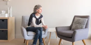 An older lady sitting on an upholstered chair.